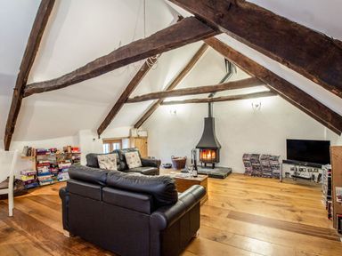 A living room with wooden beams a wood stove a tv and leather sofas at The Milking Parlour in Highampton