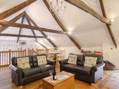 A sitting area with two black leather sofas and a wooden chest as a coffee table under exposed wooden beams at The Milking Parlour in Highampton