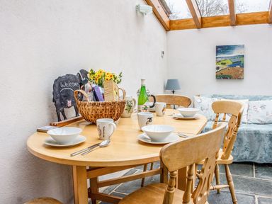 A wooden dining table set with bowls mugs cutlery and a basket of food items near a sofa with cushions in a room with skylight at The Milking Parlour in Highampton