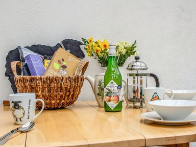 A table with a basket of food items a bottle of apple juice a French press mugs bowls and flowers at The Milking Parlour in Highampton