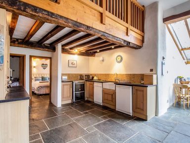 A kitchen with wooden beams overhead wooden cabinets a stove a microwave a dishwasher a sink and a dining table with chairs at The Milking Parlour in Highampton