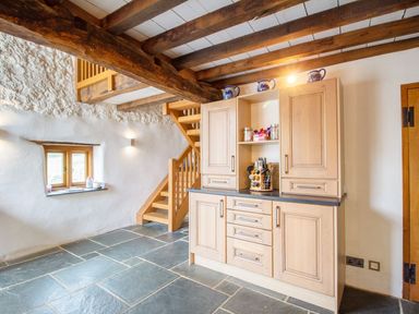 A kitchen area with wooden cabinets and stone floor near wooden stairs at The Milking Parlour in Highampton