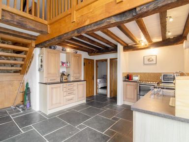 A kitchen with wooden cabinets a stove microwave and stone floor with wooden beams on the ceiling at The Milking Parlour in Highampton