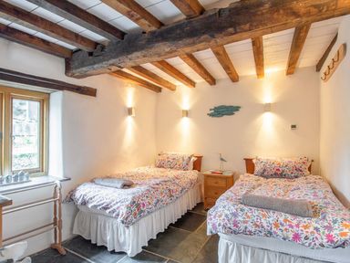 A bedroom with two single beds with floral bed covers and a wooden nightstand between them at The Milking Parlour in Highampton