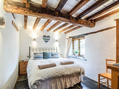 A bedroom with a bed a window wooden beams on ceiling and a wooden chair at The Milking Parlour in Highampton
