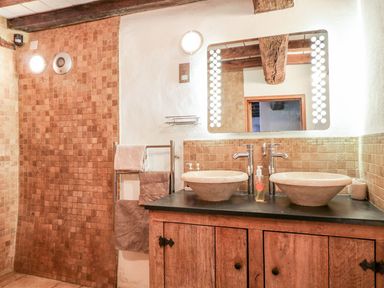 A bathroom with two vessel sinks on a wooden cabinet a mirror with lights around it and a tiled wall at The Milking Parlour in Highampton