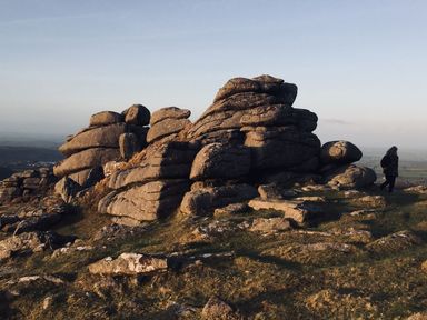 A rocky hilltop with large stacked boulders and a person walking nearby at The Milking Parlour in Highampton