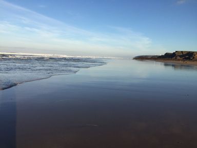 A beach with waves and cliffs under a blue sky at The Milking Parlour in Highampton
