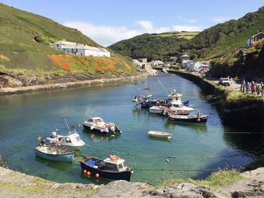 A small harbor with boats on water surrounded by hills and buildings with people walking on the shore at The Milking Parlour in Highampton