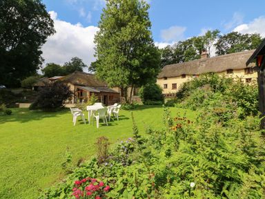 A garden with plastic chairs and a table on grass near plants and houses with thatched roofs at The Milking Parlour in Highampton