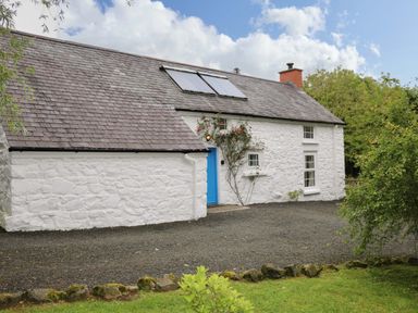 A cottage with a blue door and solar panels at Rosslare Cottage in Broughshane