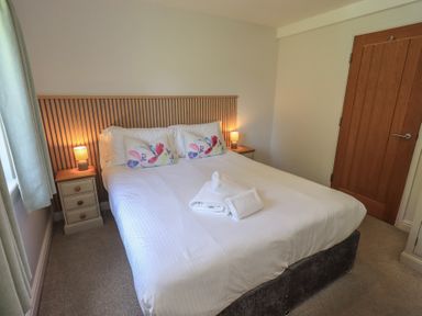 A bedroom with bed and bedside table at Yew - Woodland Cottages in Bowness-On-Windermere
