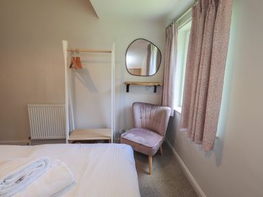 A bedroom with a bed, chair, clothing rack, and mirror at Yew - Woodland Cottages, Bowness-On-Windermere
