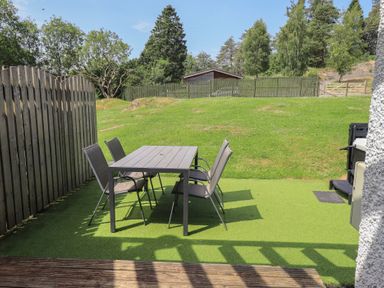 A table and chairs on grass with a shed in the background at Yew - Woodland Cottages Bowness-On-Windermere