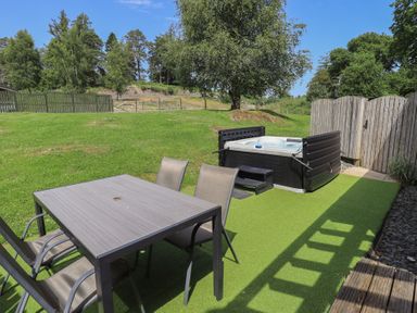 A garden with a table and chairs next to a hot tub at Yew - Woodland Cottages in Bowness-On-Windermere