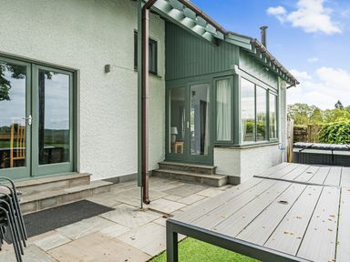 An outdoor patio with stone steps and a table next to a white and green house at Beech - Woodland Cottages in Bowness-on-Windermere