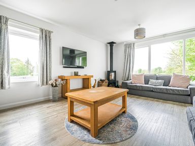 A living room with a wooden coffee table a grey sofa a wall-mounted tv and a stove at Beech - Woodland Cottages in Bowness-on-Windermere
