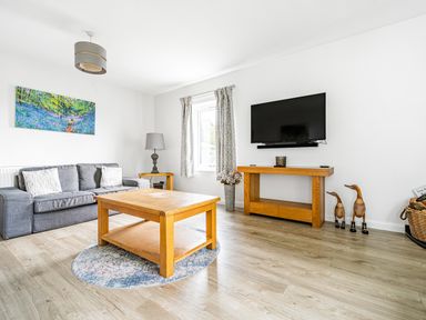 A living room with a gray sofa wooden tables a flat screen tv and decorative items at Beech - Woodland Cottages in Bowness-on-Windermere