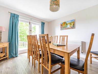 A dining room with wooden table and chairs near glass doors with blue curtains at Beech - Woodland Cottages in Bowness-on-Windermere