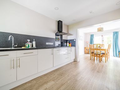 A kitchen with white cabinets and black countertop connected to a dining area with wooden table and chairs at Beech - Woodland Cottages in Bowness-on-Windermere