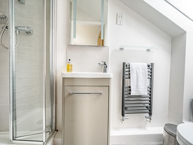 A bathroom with a shower enclosure white sink cabinet towel warmer with white towel and a trash bin at Beech - Woodland Cottages in Bowness-on-Windermere
