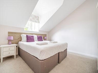 A bedroom with a double bed two purple pillows and two purple lamps on white nightstands at Beech - Woodland Cottages in Bowness-on-Windermere