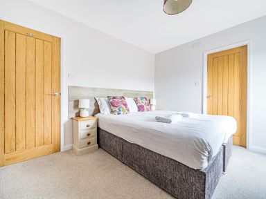 A bedroom with a double bed two wooden doors a bedside table with lamp and decorative pillows at Beech - Woodland Cottages in Bowness-on-Windermere