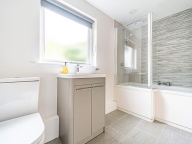 A bathroom with a toilet, sink with cabinet, and bathtub with shower and glass screen at Beech - Woodland Cottages in Bowness-on-Windermere