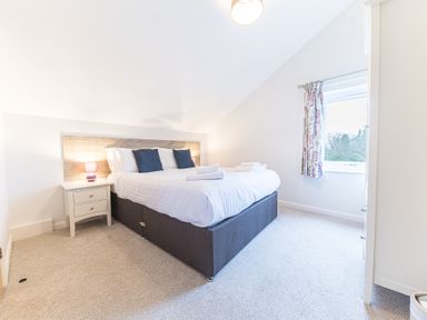 A bedroom with a double bed side tables a window and curtains at Beech - Woodland Cottages in Bowness-on-Windermere