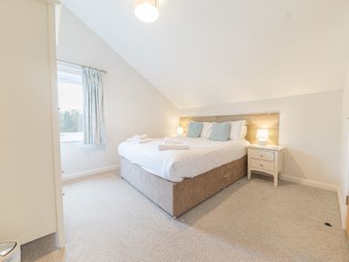 A bedroom with a double bed bedside tables lamps a window with curtains and a wardrobe at Beech - Woodland Cottages in Bowness-on-Windermere