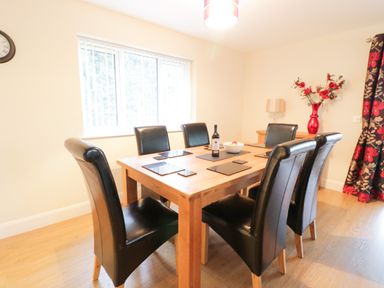 A dining room with a wooden table and six black leather chairs at Arnant in Barmouth