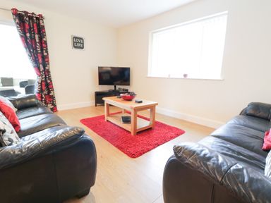 A living room with two black leather sofas a wooden coffee table on a red rug a wall mounted TV and floral curtains at Arnant in Barmouth