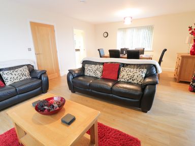 A living room with black leather sofas, a wooden coffee table, a red rug, and a dining area with a wooden table and black chairs at Arnant in Barmouth