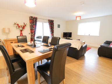 A dining area with a wooden table and black chairs next to a living room with black sofas and a TV at Arnant in Barmouth
