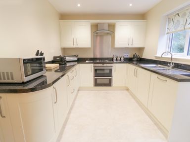 A kitchen with white cabinets black countertops a microwave toaster kettle and a double oven at Arnant in Barmouth
