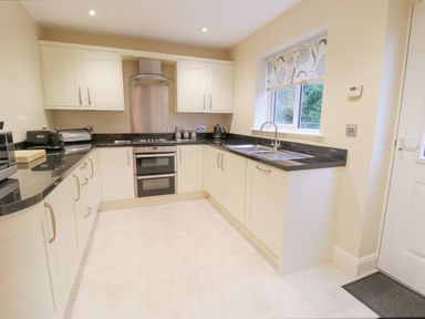 A kitchen with cream cabinets black countertops a stove and oven a sink under a window and various small appliances at Arnant in Barmouth