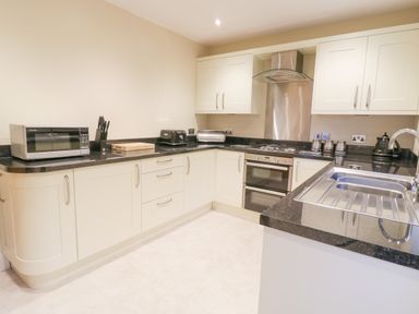 A kitchen with white cabinets black countertops a microwave toaster knives and a stainless steel sink at Arnant in Barmouth