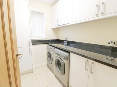 A laundry room with a washing machine and dryer under a black countertop with white cabinets at Arnant in Barmouth