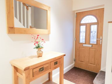 An entryway with a wooden door a wooden table with drawers a vase with flowers and a wall mirror at Arnant in Barmouth