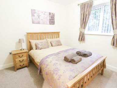 A bedroom with a wooden double bed with beige and purple bedding and a nightstand with a lamp at Arnant in Barmouth