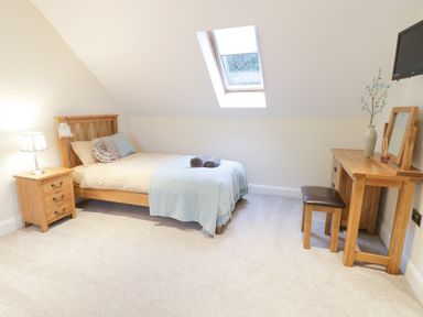 A bedroom with a single bed, bedside table with lamp, wooden dressing table with mirror, stool, and a skylight window at Arnant in Barmouth