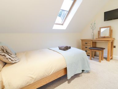 A bedroom with a bed under a skylight window and a wooden dressing table with a mirror and stool at Arnant in Barmouth