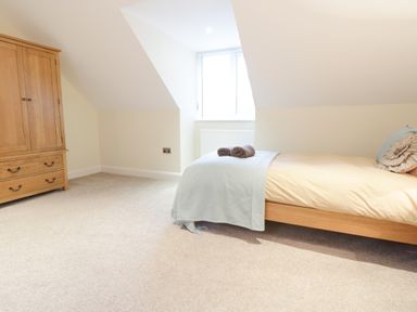 A bedroom with a single bed with pillows and folded towels next to a wooden wardrobe at Arnant in Barmouth