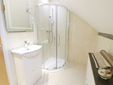 A bathroom with a shower enclosure a sink with cabinet a mirror and towels on a countertop at Arnant in Barmouth
