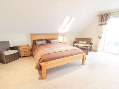 A bedroom with a wooden bed and brown bedding two wicker chairs a wooden nightstand a lamp and a skylight window at Arnant in Barmouth