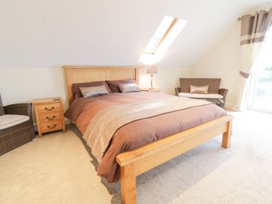 A bedroom with a wooden bed and brown bedding a bedside table with a lamp and two wicker chairs one near the bed and one near a window at Arnant in Barmouth