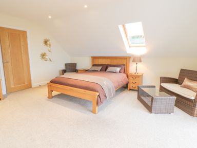 A bedroom with a wooden bed a wicker sofa and chairs a glass coffee table and a skylight window at Arnant in Barmouth