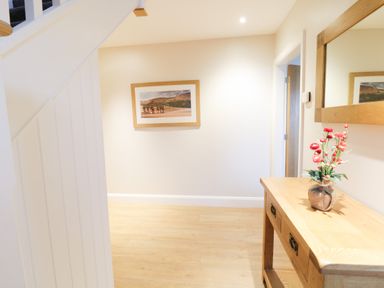 A hallway with wooden flooring a wooden console table with a vase of flowers a large wall mirror and a framed picture on the wall at Arnant in Barmouth
