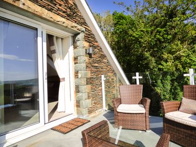 An outdoor patio area with wicker chairs and a glass table next to a stone wall and glass door at Arnant in Barmouth