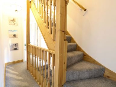 A staircase with wooden handrail in a hallway at Fern Cottage Heacham